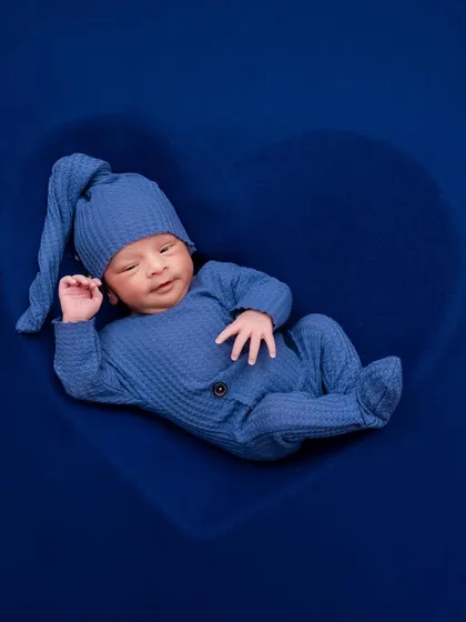 A newborn boy in a blue outfit rests inside a heart-shaped prop, looking calm and content. A simple yet powerful image.