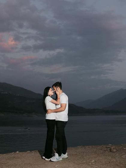 An evening shot of the couple embracing by the lake. The twilight sky and calm water create a moody and deeply romantic atmosphere.