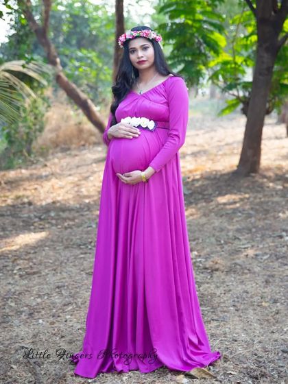 A full-length portrait in a forest setting. The mom-to-be looks serene and beautiful in a magenta gown, accented with a floral crown and belt.