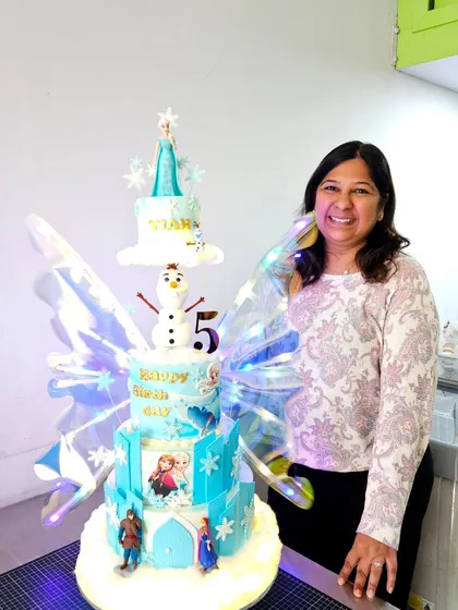 Posing with one of my most ambitious creations, a massive Frozen-themed anti-gravity cake with light-up wings. These are the challenges that push me to grow.