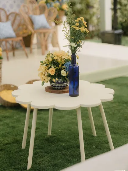 A small, flower-shaped table with a blue vase and yellow flowers, part of the chic Mediterranean-themed Haldi decor.