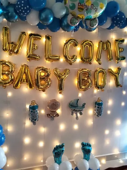 A 'Welcome Baby Boy' wall decoration with blue and white balloons, a fairy light backdrop, and baby-themed foil balloons.