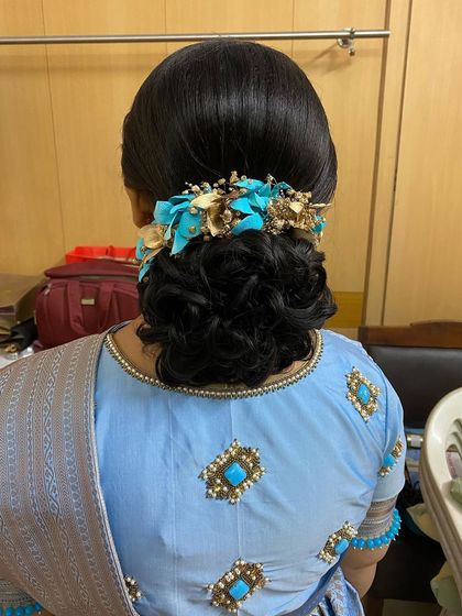 A messy bun decorated with a custom blue and gold floral accessory, designed to match the client's outfit.