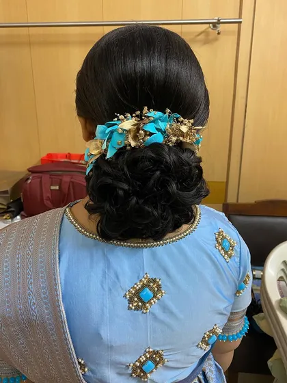 A messy bun decorated with a unique blue and gold floral accessory. This is a stylish and modern updo that adds a pop of color to the bridal look.