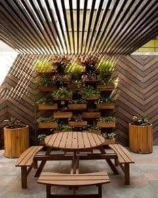 An inspiring example of a sustainable outdoor space created with wooden elements. It features a vertical garden wall, a picnic-style table and benches, and slatted walls and ceiling, showcasing how natural materials can create a modern and eco-friendly environment.