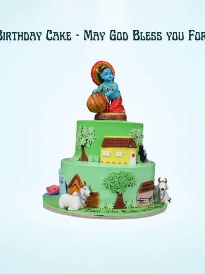 A beautiful two-tiered cake with a Little Krishna theme. The cake depicts scenes from Krishna's childhood, complete with cows and a house, perfect for a religious or cultural celebration.