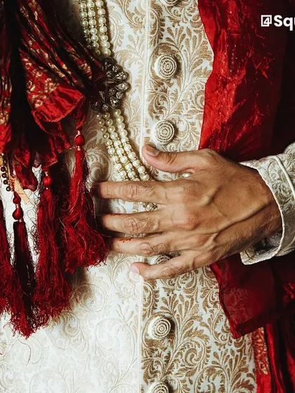 The finest details define our craftsmanship. This close-up highlights the intricate brocade fabric, custom-wound buttons, and the rich texture of a handcrafted groom's sherwani, showcasing the quality that goes into every piece.