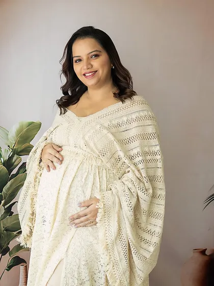A warm, welcoming smile. This mom-to-be is glowing in a beautiful cream-colored lace dress, embodying the gentle and nurturing spirit of motherhood.