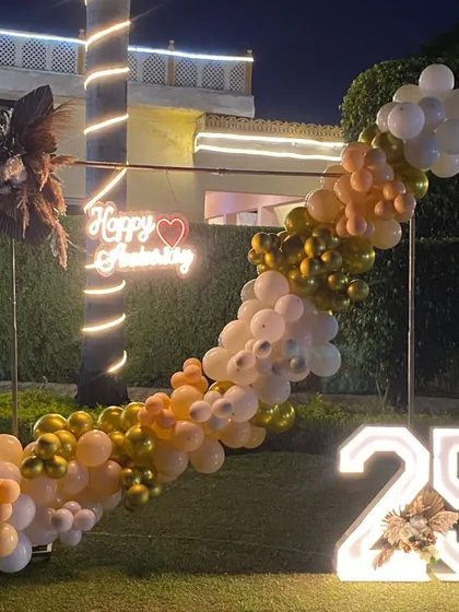 The warm lighting on the palm tree complements the golden tones of the balloon garland in this stylish outdoor anniversary decoration.