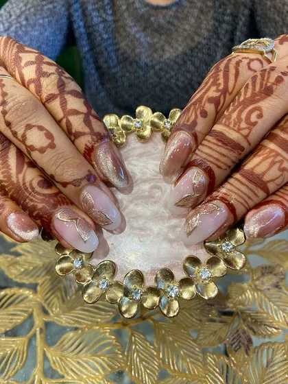 A sophisticated bridal or festive design on henna-stained hands, featuring a soft cat eye effect and delicate gold leaf accents.