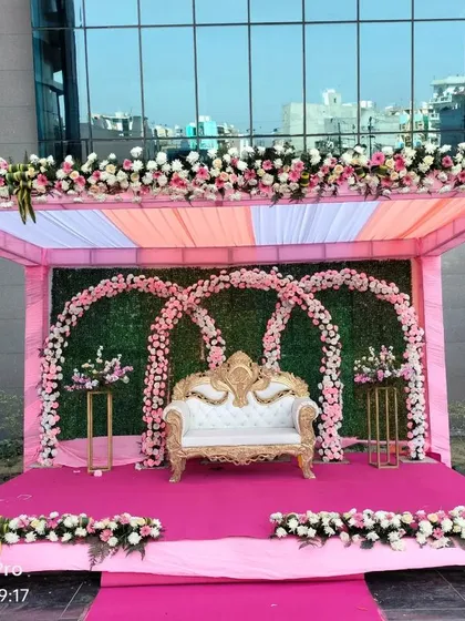 A close-up of the main wedding stage, featuring a beautiful white and gold throne-style sofa. The backdrop is a wall of greenery with three floral arches.
