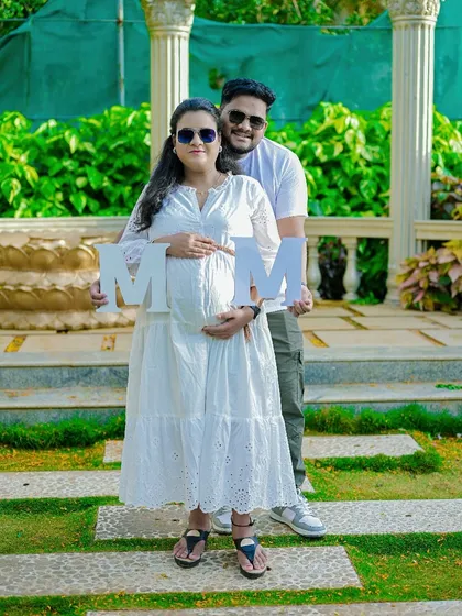 A fun and modern outdoor portrait. The couple holds up letters, adding a personal and creative touch to their pregnancy announcement photo.