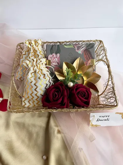 A simple yet elegant Diwali gift tray. The golden wire basket holds a potli bag of goodies and a decorative diya, accented with deep red roses for a festive touch.