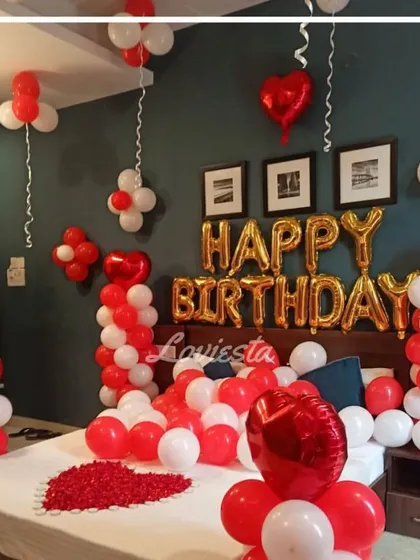 Here is one of my classic romantic birthday room decorations. The room is filled with red and white balloons on the ceiling and floor, 'Happy Birthday' foil letters above the bed, and a heart made of rose petals on the bed itself.