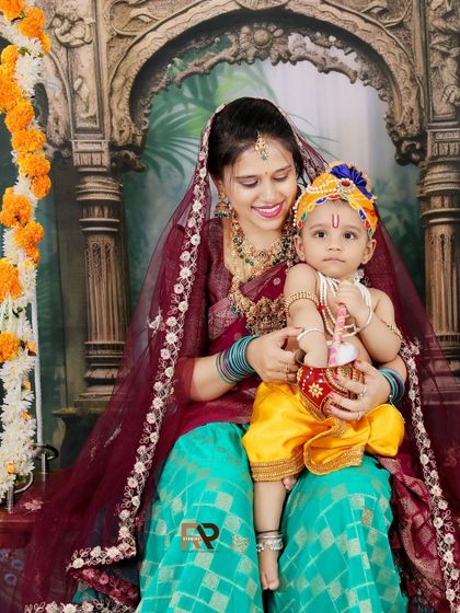 A mother dressed as Radha holds her baby, who is dressed as Little Krishna. This is a beautiful way to include parents in themed photoshoots and create lasting memories.