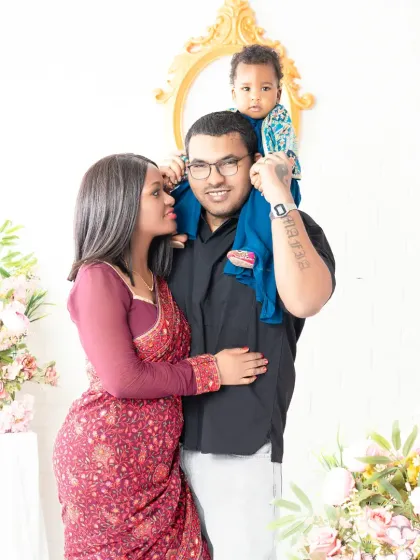 A loving family of three posing for a classic portrait. The father gives his child a shoulder ride while the mother looks on with affection, creating a beautiful and connected family image.
