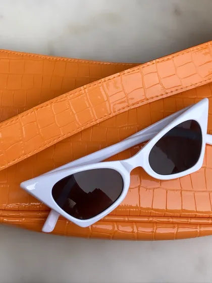 A classic pairing for a sunny day. A vibrant neon orange baguette bag and chic white cat-eye sunglasses are the only accessories you need to make a simple outfit pop.