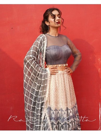 This grey and cream georgette lehenga features intricate all-over threadwork. The look is completed with a matching dupatta and a stylish raw silk and tulle crop top.