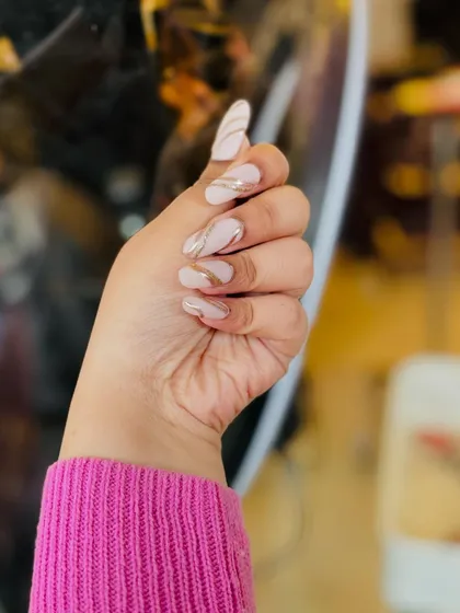 A side view of the elegant manicure with a milky nude base and delicate gold line art. This angle shows the graceful curve of the long almond nails.