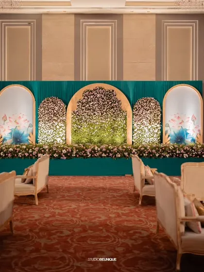 A stunning reception stage with a deep teal backdrop and arches filled with flowers. The design is modern yet timeless, providing a sophisticated setting for the couple.