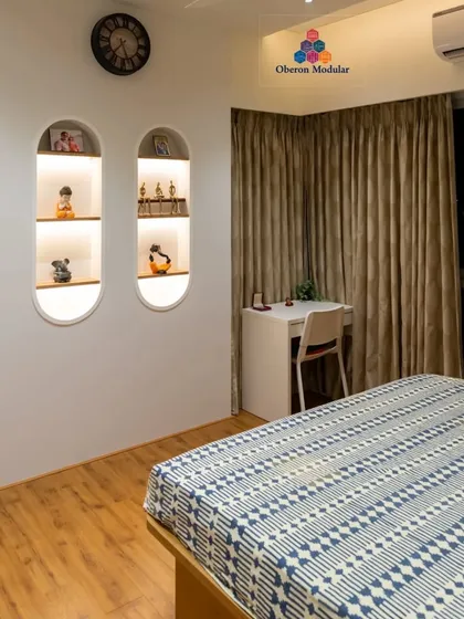 This bedroom combines functionality and style with a built-in study desk and illuminated display niches. The wooden flooring and warm lighting create a cozy and productive environment.