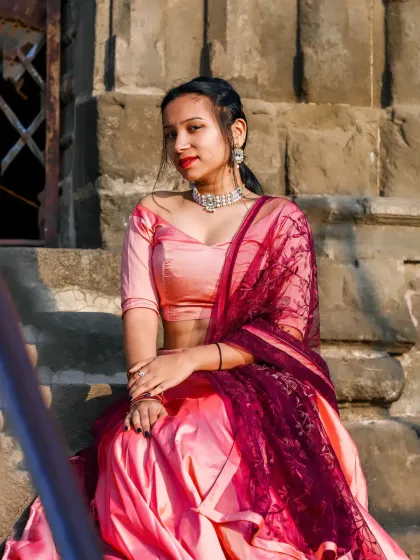 A beautiful portrait of a woman in a pink and maroon lehenga, seated on ancient stone steps, creating a look of royal elegance.