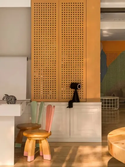 Another view of the playful seating and storage. The mix of natural wood tones, pops of color on the chairs, and the texture of the perforated screen creates a multi-sensory and engaging environment for young patients.