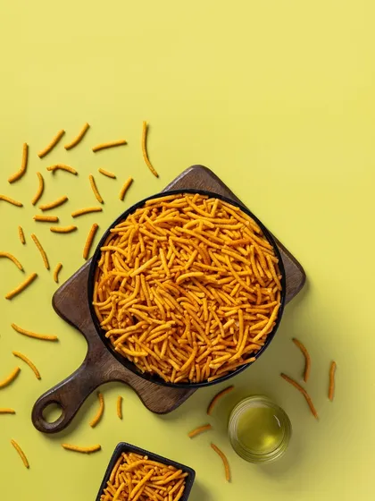A top-down shot of spicy sev on a yellow background. The composition leaves ample copy space, making it a versatile asset for packaging and advertising.
