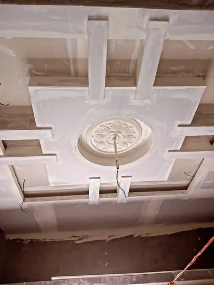 An unpainted POP ceiling showing a classic design with a central floral medallion. The wiring for the central light fixture is already in place.