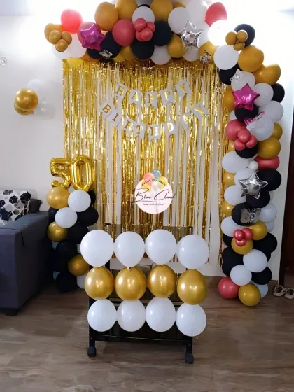 A grand 50th birthday celebration with a black, gold, and white balloon arch and shimmer curtain.