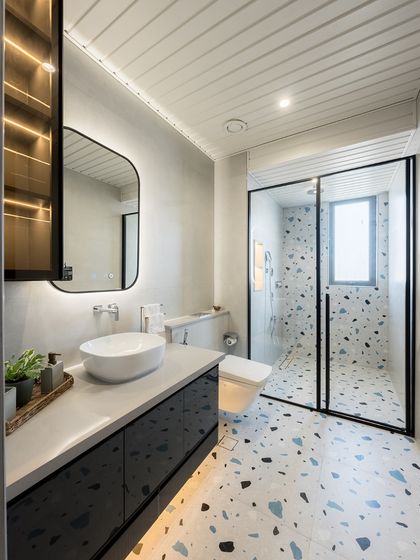 This bathroom features playful terrazzo flooring that extends into the shower. A sleek, dark vanity and an illuminated mirror complete the modern, stylish look.