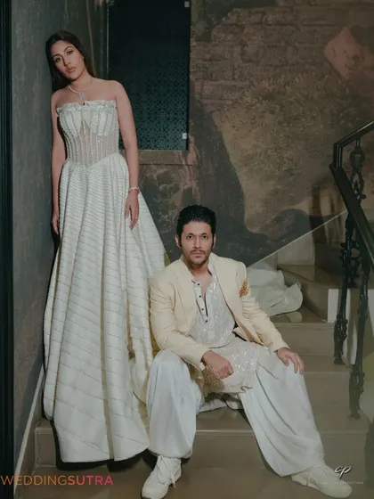 A stylish, full-length portrait on a staircase, showcasing the couple's designer outfits. The composition and posing give this pre-wedding photo a modern and editorial feel.
