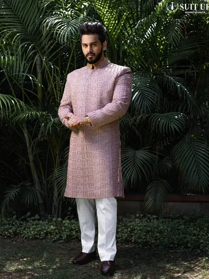 A full-length shot of a client in a mauve sherwani with all-over embroidery, paired with classic white trousers. A sophisticated and unique color choice for a wedding event.