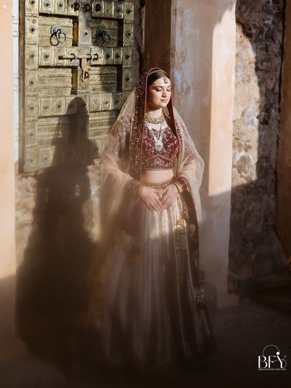 A bride stands in a sunbeam against an old wooden door, the light creating a magical, painterly effect.