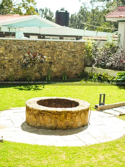 A classic stone well serves as a rustic centerpiece in this sunny backyard, surrounded by a circular stone patio and a healthy green lawn.
