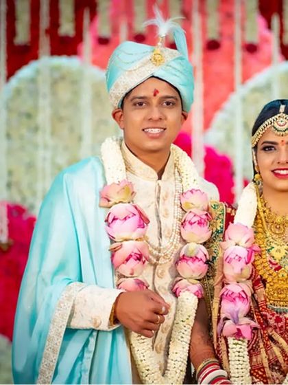A classic wedding portrait of a couple adorned with beautiful lotus garlands, posing against a floral backdrop.