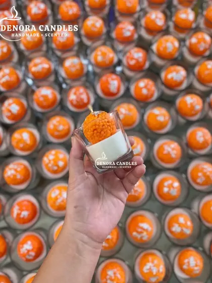 A single laddoo candle held up to show the detail, with the larger batch in the background.