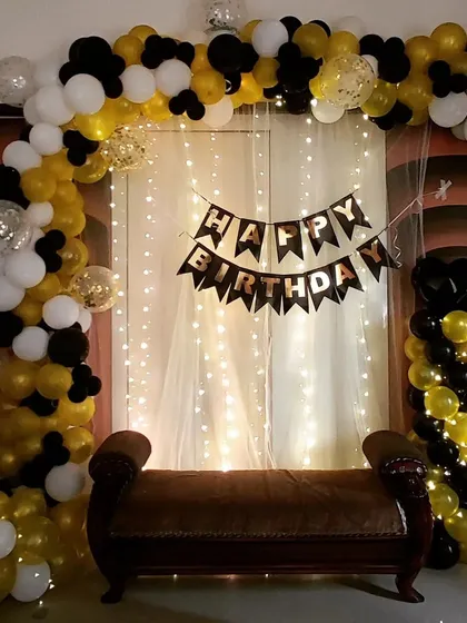 A classic black, white, and gold balloon arch against a fairy light curtain. This setup provides an elegant and timeless backdrop for any birthday celebration.