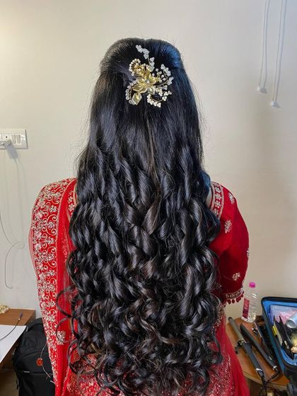 A reception hairstyle with long, defined curls and a half-updo, adorned with a sparkling gold and pearl accessory.