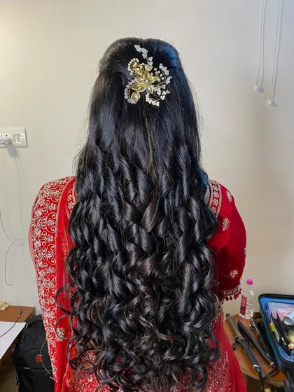 A beautiful half-updo with long, flowing curls, adorned with a delicate pearl accessory. This is a timeless and elegant choice for a reception or engagement.