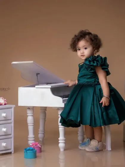 A little pianist in the making. This toddler in a beautiful green dress stands at a miniature white piano, creating an elegant and adorable portrait.