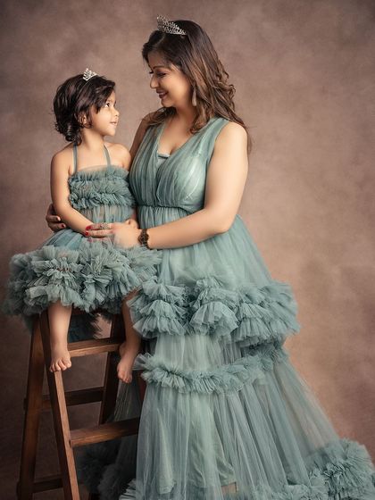 A mother and daughter share a quiet look of love. The matching sage green gowns and tiaras create a beautifully coordinated and elegant portrait.