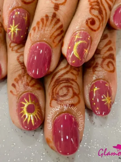Celestial-themed nails for a festive celebration. This design features a rich mauve base adorned with hand-painted golden sun, moon, and star motifs that beautifully complement the henna.