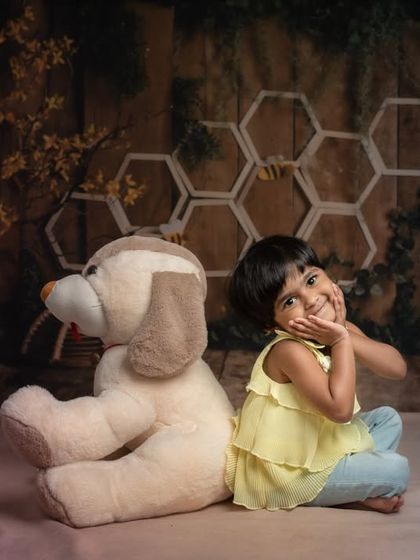 A sweet and shy pose from a toddler during her creative studio photoshoot. Surrounded by stacks of books and her favorite stuffed animal, she shows off her charming personality.