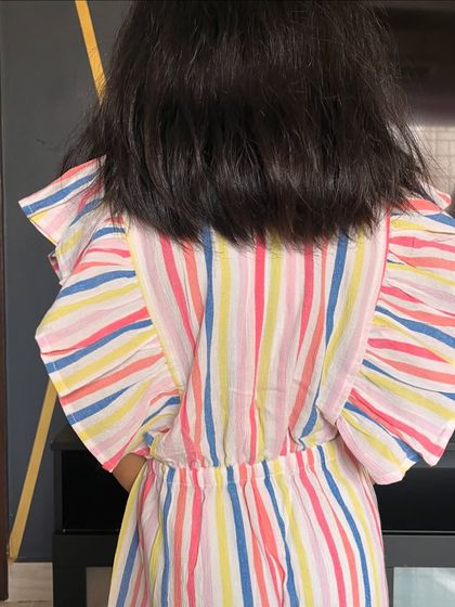 A view of the back of our rainbow striped jumpsuit. The flutter sleeves are just so sweet, and the cotton fabric is incredibly soft and breathable.