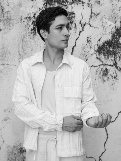 A relaxed, candid-style portrait against a textured, cracked wall. This black and white shot has a timeless, documentary feel, focusing on the model in a natural state.