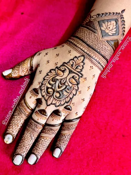 A light and elegant back-of-hand design featuring two peacocks in a crest-like shape. The delicate finger work complements the central motif.