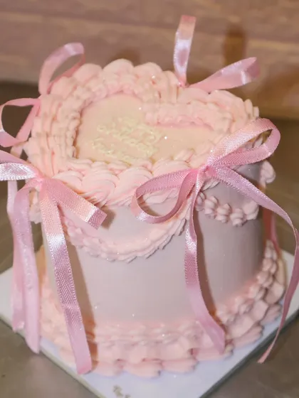 A dreamy pastel pink heart-shaped cake, covered in sparkles and decorated with intricate piping and dainty pink bows for a magical birthday.
