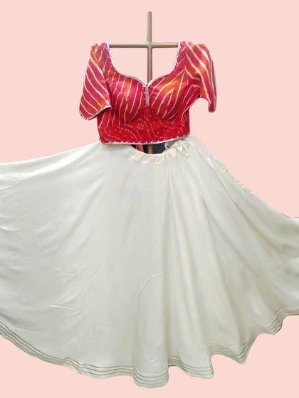 This white lehenga skirt provides a perfect canvas for the vibrant red bandhani and leheriya print blouse. The flared skirt is light and ideal for twirling during garba.