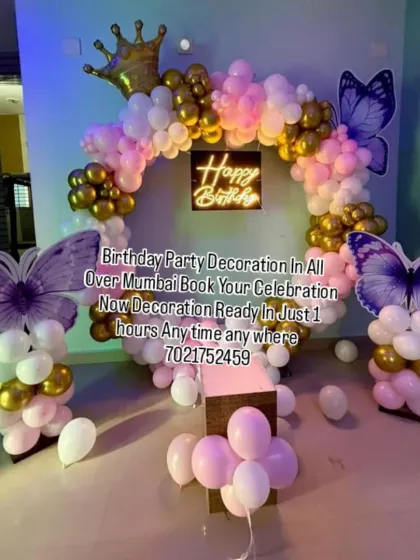 This butterfly-themed decoration uses large purple butterfly wings as statement pieces. The pink, white, and gold balloon ring and neon sign complete this eye-catching setup.